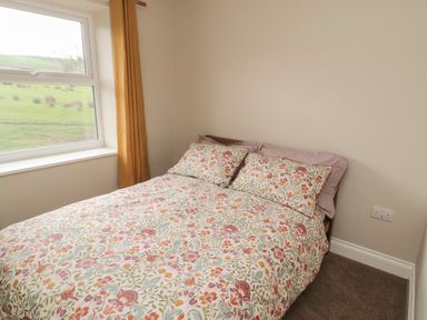 A bedroom with a bed with floral bedding beside a window with mustard curtains at The Hollow in West Woodburn