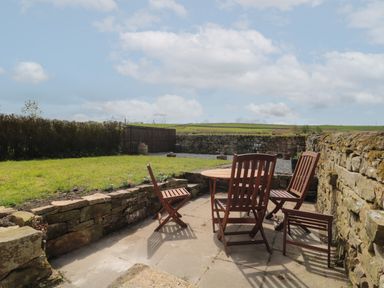 An outdoor patio area with wooden chairs and a round table next to stone walls and a grassy yard at The Hollow in West Woodburn