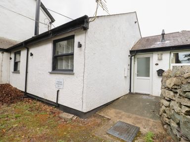 Exterior view of a building with two black framed windows a white door and a stone wall at Fir Tree Cottage in Llanrug