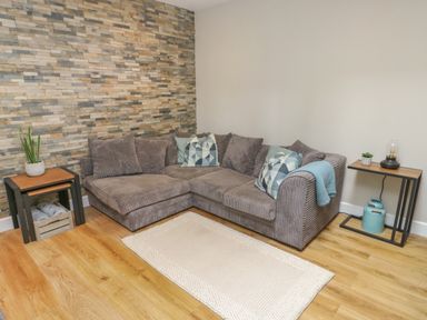 A corner sofa with cushions and a rug on a wooden floor next to two side tables in a living room at Fir Tree Cottage in Llanrug