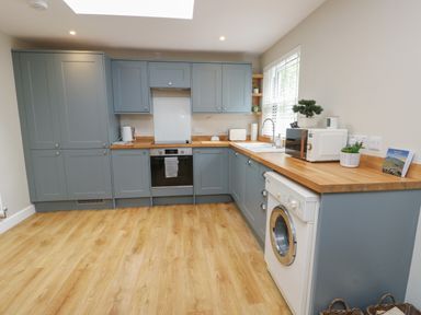 A kitchen with blue cabinets wooden countertops washing machine oven microwave and a window at Fir Tree Cottage in Llanrug