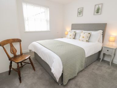 A bedroom with a bed with pillows and a blanket two bedside tables with lamps a window with blinds and a wooden chair at Fir Tree Cottage in Llanrug