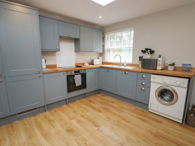 A kitchen with blue cabinets wooden countertops a washing machine oven microwave and a window with blinds at Fir Tree Cottage in Llanrug