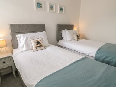 A bedroom with two single beds with grey headboards and bee cushions at Fir Tree Cottage in Llanrug