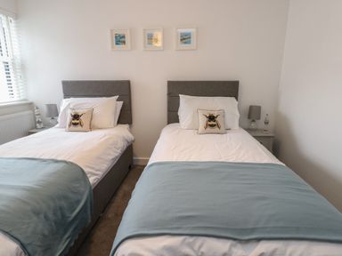 A bedroom with two single beds with grey headboards and blue throws at Fir Tree Cottage in Llanrug