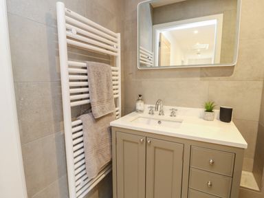 A bathroom with a sink cabinet a mirror a heated towel rack with towels and a soap dispenser at Fir Tree Cottage in Llanrug