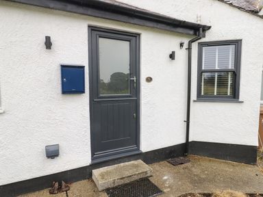 An exterior door with a glass panel next to a blue mailbox and window with blinds at Bay Tree Cottage in Llanrug