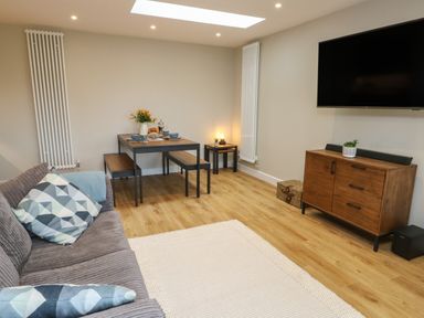 A living room with a sofa pillows dining table bench wooden cabinet and wall mounted tv at Bay Tree Cottage in Llanrug