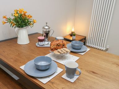 A wooden dining table with blue bowls plates and mugs bread jam coffee press and flowers at Bay Tree Cottage in Llanrug