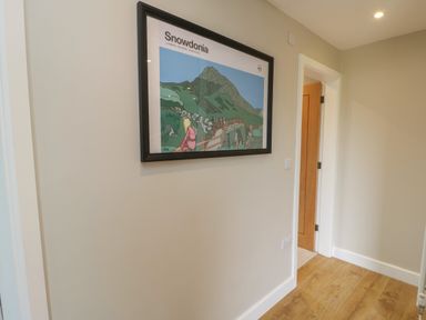 A hallway with a framed picture of Snowdonia on the wall and an open door leading to another room at Bay Tree Cottage in Llanrug