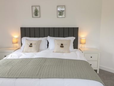 A bedroom with a double bed with bee pillows two bedside tables with lamps and botanical prints on wall at Bay Tree Cottage in Llanrug