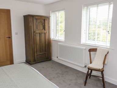 A bedroom with a wooden wardrobe wooden chair with a blanket and two windows at Bay Tree Cottage in Llanrug