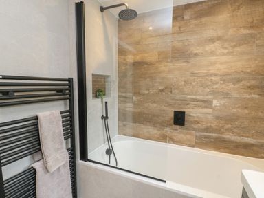 A bathroom with a bathtub shower combination and towel rail at Bay Tree Cottage in Llanrug