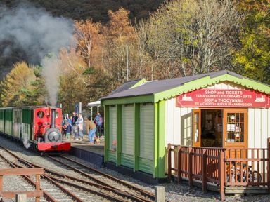 A small train station with a red steam train arriving and a ticket shop next to the platform at Bay Tree Cottage in Llanrug