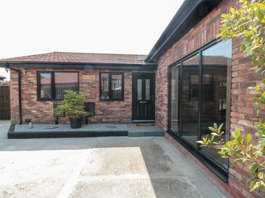 Exterior view of a brick house with a black front door windows a potted plant and a concrete driveway at 31A The Green in Scalby