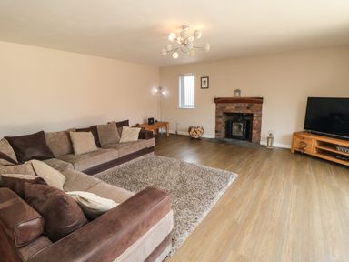 A living room with a brown sectional sofa a rug a brick fireplace and a television on a wooden stand at 31A The Green in Scalby