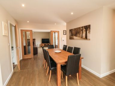 A dining room with a wooden table and eight black chairs near a living room at 31A The Green in Scalby