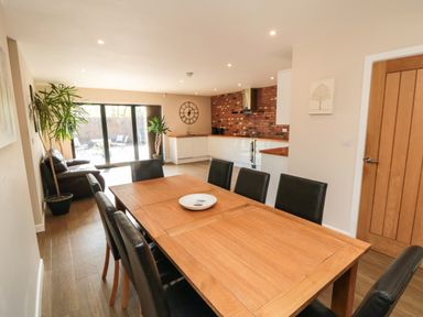 A dining area with wooden table and black chairs next to a kitchen with white cabinets and a brick backsplash at 31A The Green in Scalby