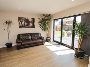 A living room with a brown leather sofa three potted plants a wall picture and large glass doors at 31A The Green in Scalby