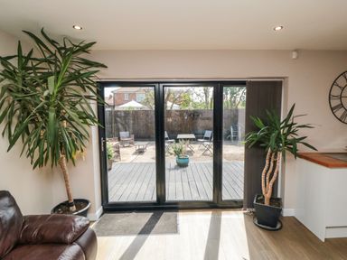 A room with large glass sliding doors leading to a patio with outdoor furniture and potted plants at 31A The Green in Scalby