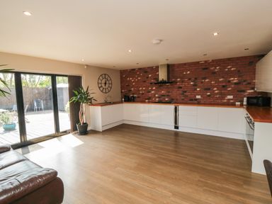 A kitchen with white cabinets wooden countertops and a brick wall with a large clock and sliding glass doors at 31A The Green in Scalby