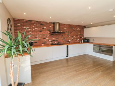 A kitchen with white cabinets a wooden countertop a brick wall a potted plant and stainless steel appliances at 31A The Green in Scalby