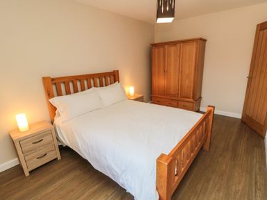 A bedroom with a wooden bed and white bedding, two wooden bedside tables with lamps, a wooden wardrobe, and a wooden door at 31A The Green in Scalby