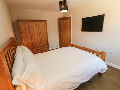 A bedroom with a wooden bed and white bedding a wooden wardrobe a wooden door and a wall mounted television at 31A The Green in Scalby