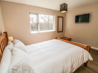 A bedroom with a wooden bed frame white bedding a window wall mirror bedside table and a wall mounted television at 31A The Green in Scalby