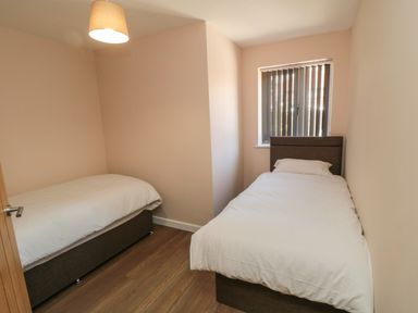 A small bedroom with two single beds a window with vertical blinds and a ceiling light at 31A The Green in Scalby