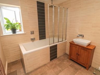 A bathroom with a bathtub and a wooden vanity with a sink and a plant on the window sill at 31A The Green in Scalby