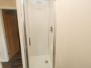 A shower enclosure with glass door and chrome fixtures next to a wooden door on a wooden floor at 31A The Green Scalby