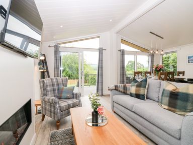 A living room and dining area with a gray sofa and checkered armchair at Eden Fields Lodge in Cupar Fife