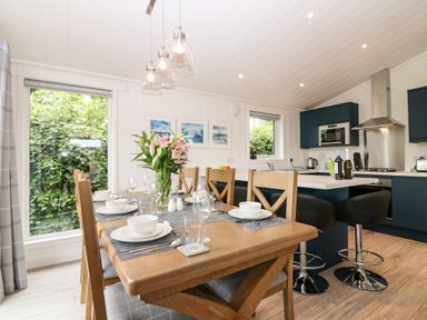 A dining area with a wooden table set with bowls glasses and a vase with flowers next to a kitchen with blue cabinets and bar stools at Eden Fields Lodge in Cupar Fife