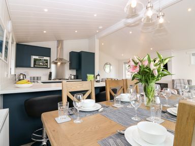 A dining table set with plates glasses and cutlery next to a kitchen with blue cabinets and a fruit bowl at Eden Fields Lodge in Cupar Fife