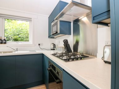 A kitchen with blue cabinets a gas stove a microwave a kettle a toaster and a sink at Eden Fields Lodge in Cupar Fife