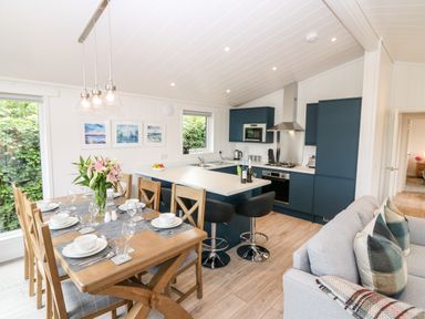 A kitchen with blue cabinets a dining table set with dishes and glasses and a grey sofa with pillows at Eden Fields Lodge in Cupar Fife