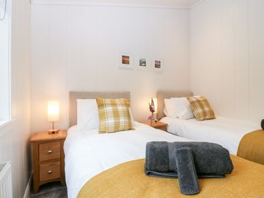 A bedroom with two single beds with white bedding and yellow plaid pillows at Eden Fields Lodge in Cupar Fife