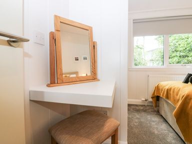 A small dressing table with a wooden framed mirror and stool next to a window in a bedroom at Eden Fields Lodge in Cupar Fife