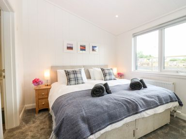 A bedroom with a double bed with blue throws and plaid pillows beside nightstands with lamps and flowers at Eden Fields Lodge in Cupar Fife