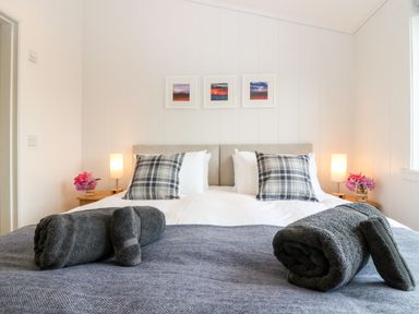 A bedroom with a double bed two plaid pillows rolled towels bedside tables with lamps and flowers three pictures above the bed at Eden Fields Lodge in Cupar Fife