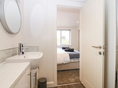 A bathroom sink with a round mirror and a view into a bedroom with a bed and window at Eden Fields Lodge in Cupar Fife