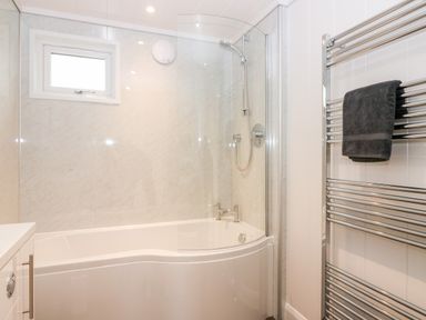 A bathroom with a white bathtub and shower combination a window a chrome towel rack with a black towel at Eden Fields Lodge in Cupar Fife