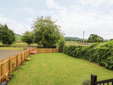 A fenced grassy backyard with flowers along the fence and trees in the background at Eden Fields Lodge in Cupar Fife