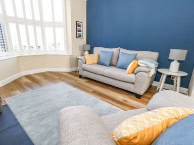 A living room with gray sofas blue and yellow cushions a round side table with a lamp and a light blue rug at Leos Place in Weymouth
