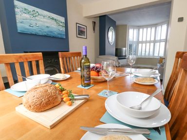 A dining table set with bowls plates glasses bread a bottle of wine and a fruit bowl in a dining room at Leos Place in Weymouth