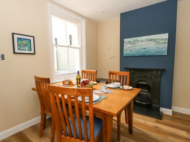 A dining room with a wooden table and chairs near a window and fireplace at Leos Place in Weymouth
