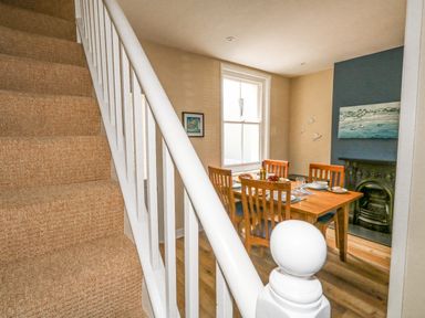 A dining room with a wooden table and chairs near a window next to a staircase at Leo's Place in Weymouth