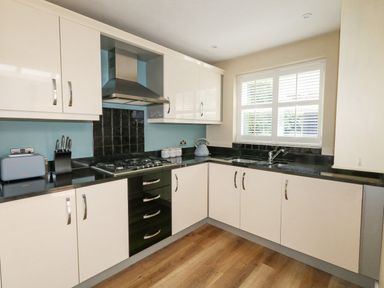 A kitchen with white cabinets black countertops a stove a blue toaster a blue kettle and a window with white shutters at Leos Place in Weymouth