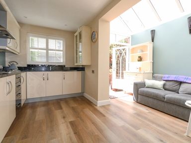 A kitchen area with white cabinets and a window next to a living space with a gray sofa and a white cabinet at Leos Place in Weymouth